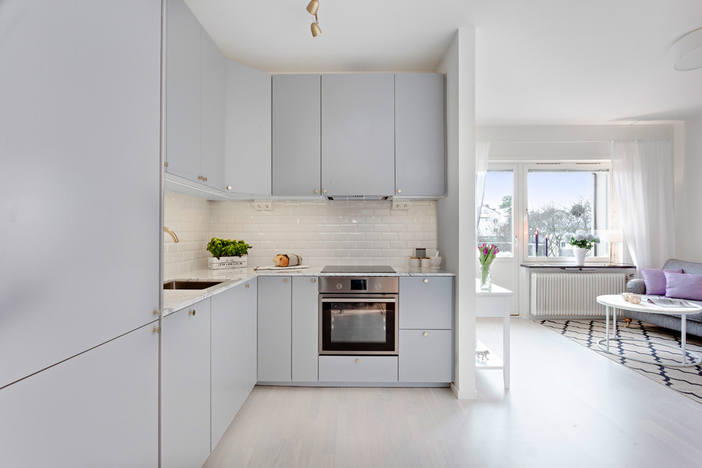 Inredning av ett modernt litet kök, med en nedsänkt diskho, grå skåp, marmorbänkskiva, vitt stänkskydd, stänkskydd i cementkakel, rostfria vitvaror och ljust trägolv