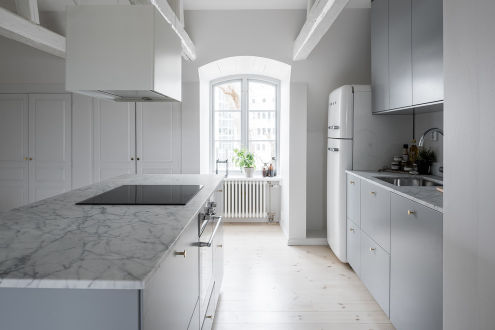 Photo of a scandinavian galley kitchen in Stockholm with a submerged sink, flat-panel cabinets, grey cabinets, white appliances, light hardwood flooring, an island, beige floors and white worktops.
