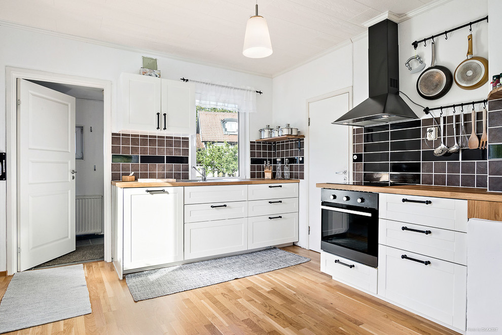 Mid-sized danish l-shaped medium tone wood floor eat-in kitchen photo in Malmo with white cabinets, wood countertops, no island, a double-bowl sink, black backsplash, ceramic backsplash and shaker cabinets