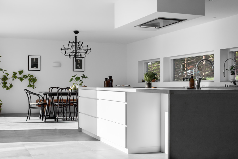 Foto på ett stort funkis grå kök, med en dubbel diskho, släta luckor, vita skåp, vitt stänkskydd, rostfria vitvaror, cementgolv, en halv köksö och grått golv