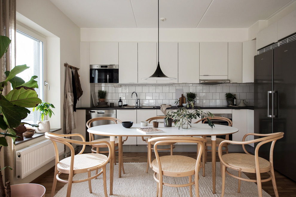 Eat-in kitchen - scandinavian l-shaped medium tone wood floor eat-in kitchen idea in Gothenburg with a double-bowl sink, flat-panel cabinets, white cabinets, white backsplash, stainless steel appliances, no island and black countertops