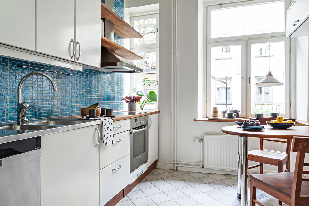 Foto på ett mellanstort funkis linjärt kök och matrum, med en integrerad diskho, släta luckor, beige skåp, bänkskiva i rostfritt stål, blått stänkskydd, stänkskydd i mosaik, rostfria vitvaror och grått golv