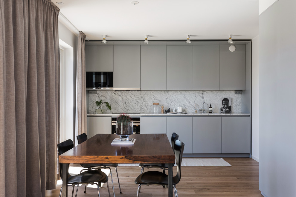 Modern inredning av ett mellanstort linjärt kök, med släta luckor, grå skåp, marmorbänkskiva, grått stänkskydd och mellanmörkt trägolv