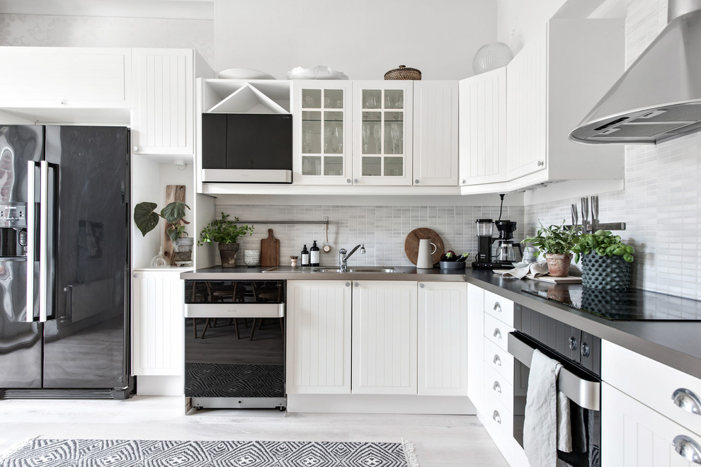 Foto på ett nordiskt grå l-kök, med en dubbel diskho, vita skåp, grått stänkskydd, svarta vitvaror, målat trägolv, vitt golv och släta luckor