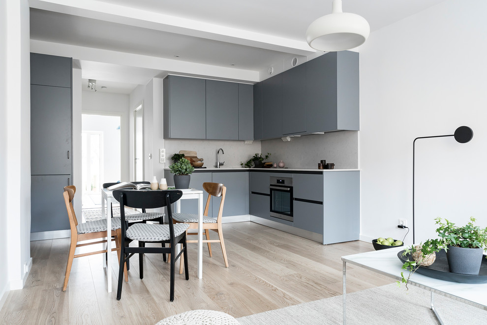 Bild på ett litet skandinaviskt l-kök, med släta luckor, grå skåp, grått stänkskydd, integrerade vitvaror, ljust trägolv och beiget golv