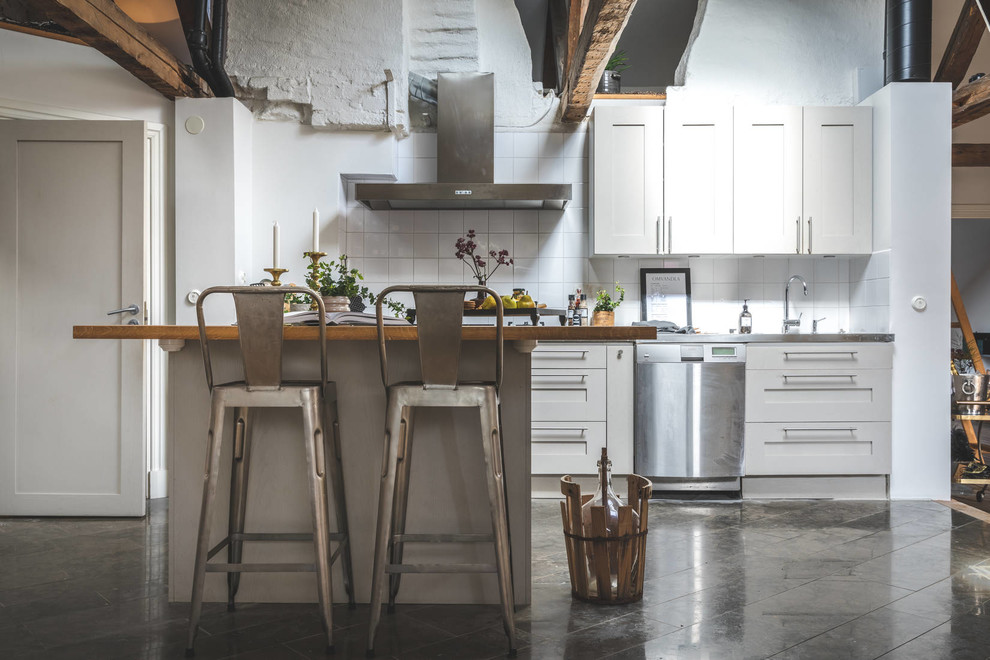 Inspiration for a mid-sized rustic gray floor kitchen remodel in Gothenburg with white cabinets, wood countertops, white backsplash, an island, brown countertops, shaker cabinets and stainless steel appliances