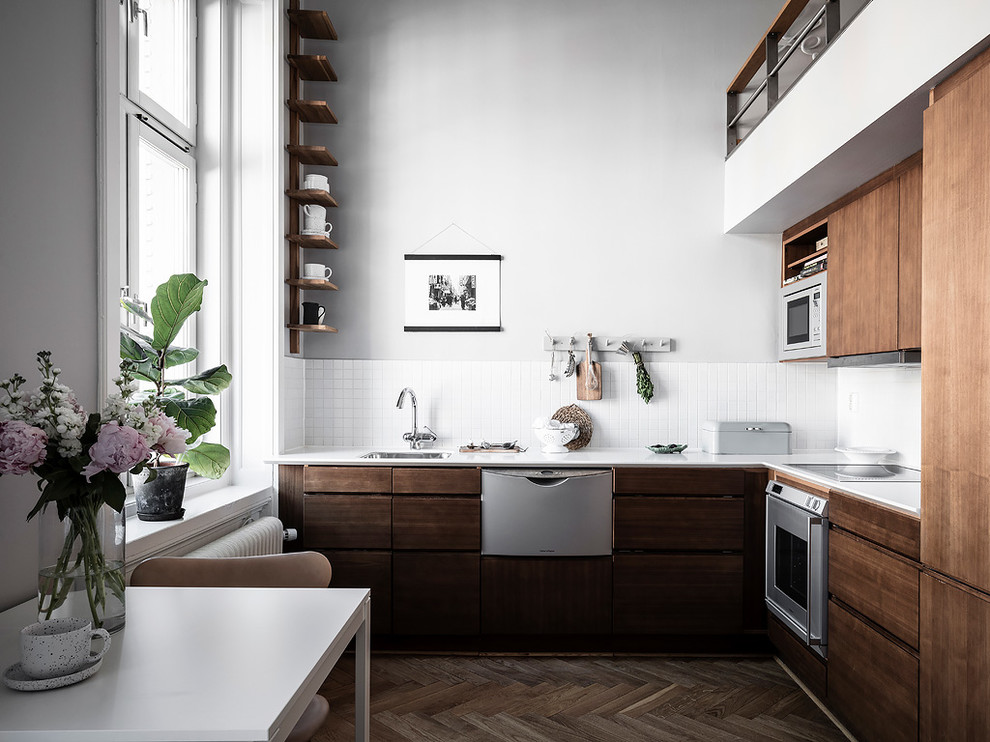 Small scandinavian l-shaped open plan kitchen in Gothenburg with a built-in sink, flat-panel cabinets, medium wood cabinets, white splashback, dark hardwood flooring, no island, brown floors and white worktops.
