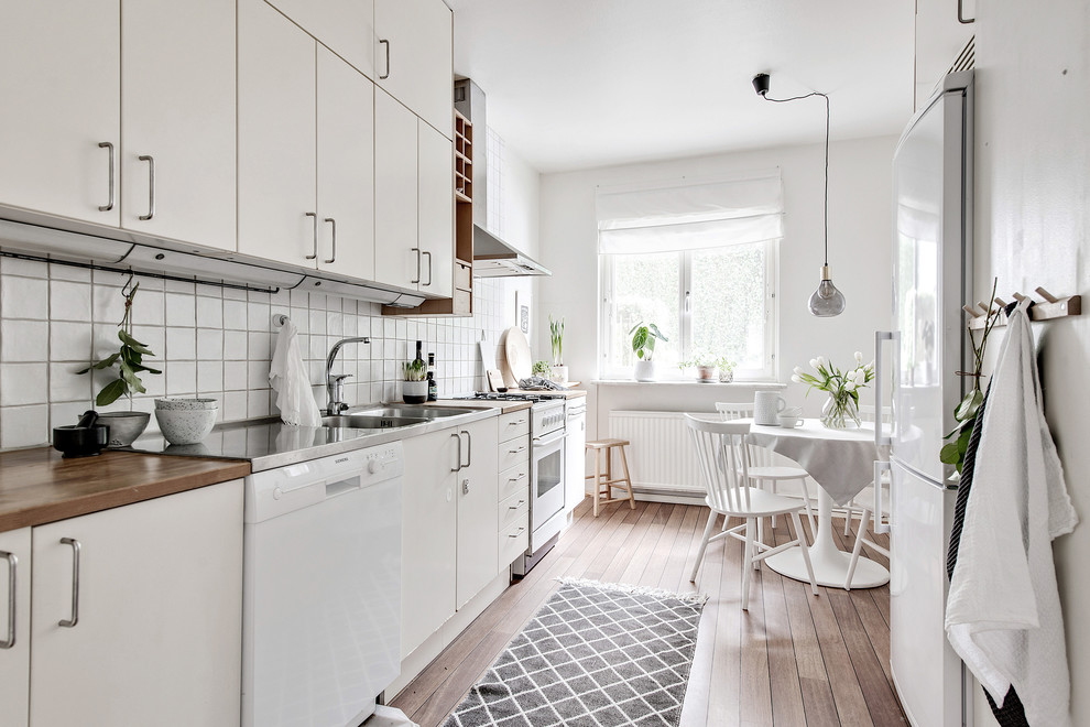Idéer för ett skandinaviskt kök, med en dubbel diskho, släta luckor, vita skåp, träbänkskiva, vitt stänkskydd, vita vitvaror, mellanmörkt trägolv och brunt golv