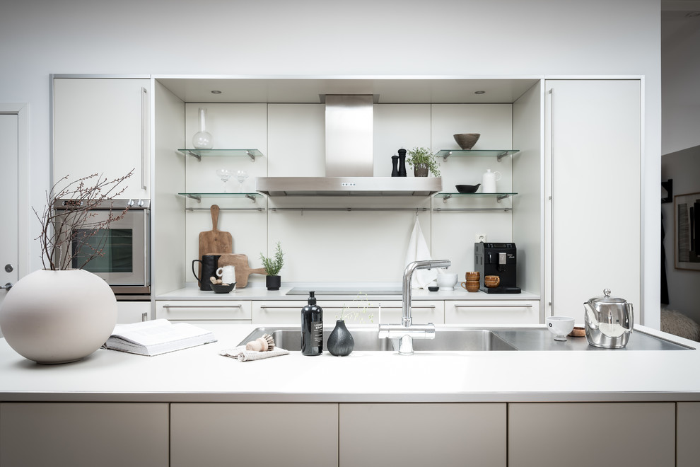 Exemple d'une cuisine scandinave avec un évier 2 bacs, un placard à porte plane, des portes de placard blanches, une crédence blanche, un électroménager en acier inoxydable, îlot et un plan de travail blanc.