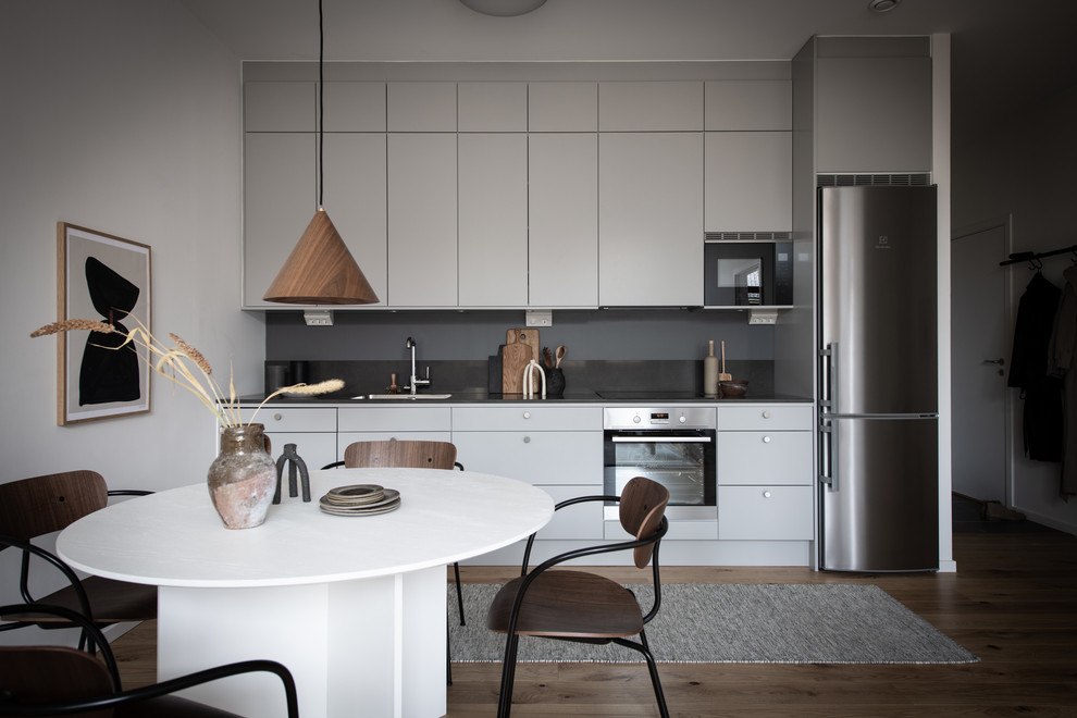 Idéer för att renovera ett skandinaviskt linjärt kök med öppen planlösning, med en integrerad diskho, släta luckor, grå skåp, bänkskiva i rostfritt stål, grått stänkskydd, rostfria vitvaror och mörkt trägolv
