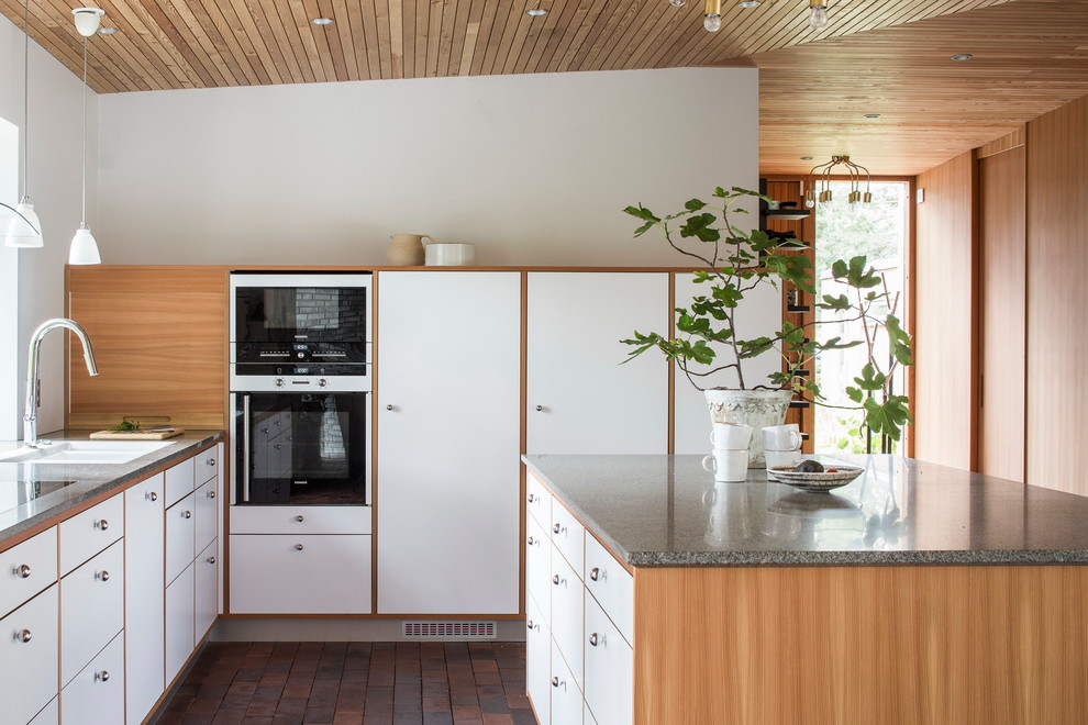 Стильный дизайн: маленькая параллельная, отдельная кухня в скандинавском стиле с двойной мойкой, плоскими фасадами, белыми фасадами, кирпичным полом, островом, гранитной столешницей и белой техникой для на участке и в саду - последний тренд
