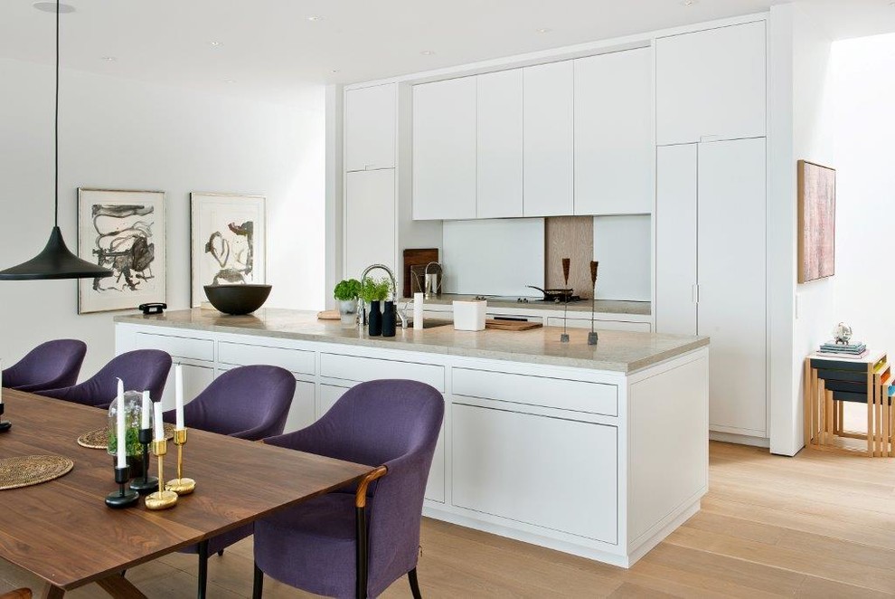 Modern inredning av ett mellanstort kök, med en undermonterad diskho, släta luckor, vita skåp, ljust trägolv, en köksö, granitbänkskiva och vitt stänkskydd