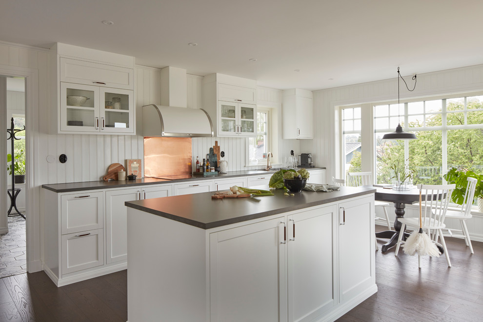 Cette image montre une cuisine américaine parallèle traditionnelle de taille moyenne avec un placard à porte shaker, des portes de placard blanches, parquet foncé, îlot et une crédence blanche.