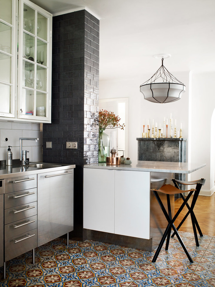Bild på ett avskilt, mellanstort nordiskt linjärt kök, med en integrerad diskho, luckor med glaspanel, vita skåp, bänkskiva i rostfritt stål, vitt stänkskydd, en halv köksö och klinkergolv i porslin