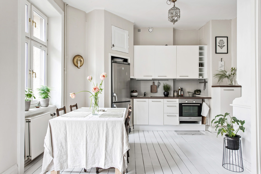 ヨーテボリにある広い北欧スタイルのおしゃれなキッチン (フラットパネル扉のキャビネット、白いキャビネット、木材カウンター、グレーのキッチンパネル、塗装フローリング、アイランドなし、白い床、茶色いキッチンカウンター、シルバーの調理設備) の写真