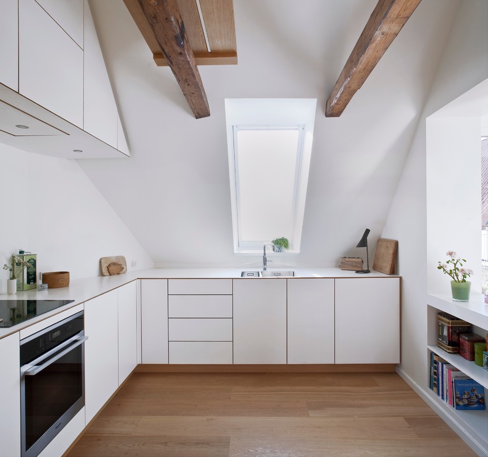 Medium sized scandi l-shaped enclosed kitchen in Copenhagen with a built-in sink, flat-panel cabinets, white cabinets, laminate countertops, stainless steel appliances, light hardwood flooring and no island.