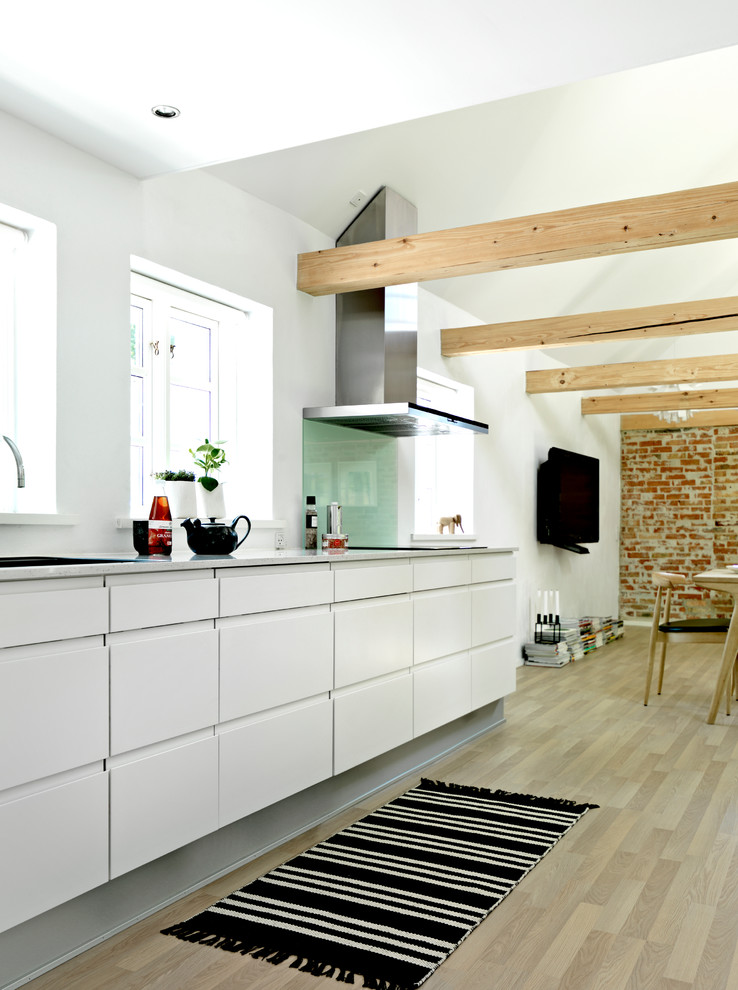 Exempel på ett mellanstort skandinaviskt linjärt kök och matrum, med en nedsänkt diskho, släta luckor, vita skåp, laminatbänkskiva, vitt stänkskydd, glaspanel som stänkskydd och ljust trägolv