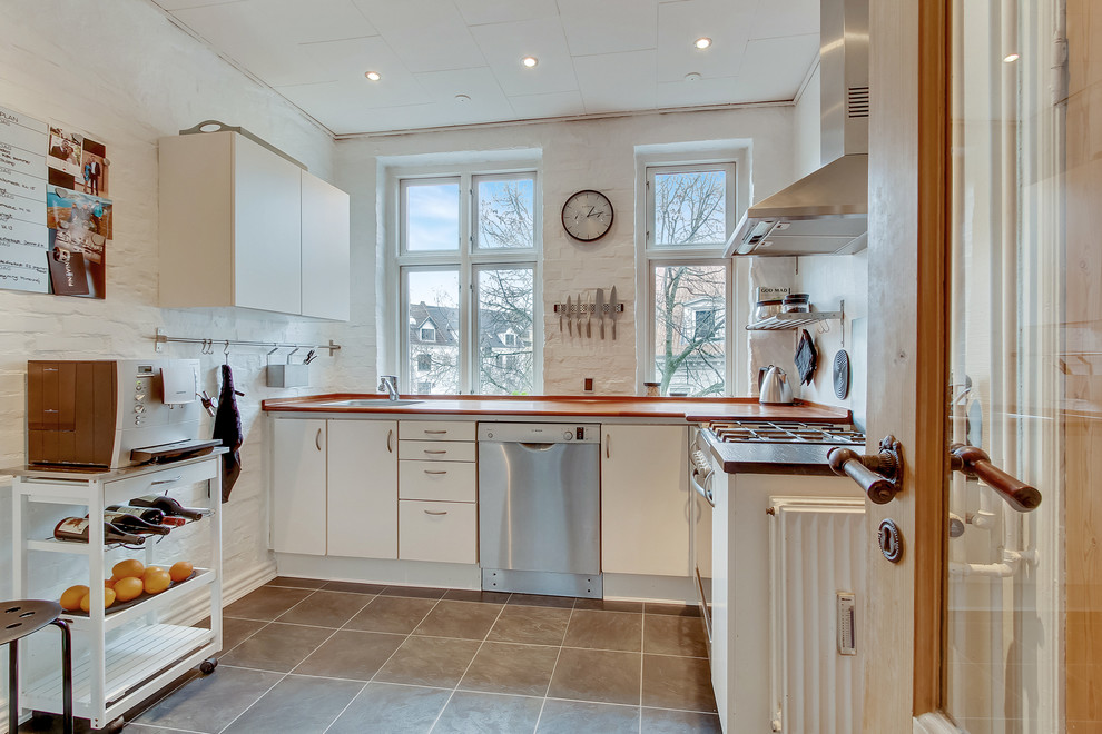 Bild på ett avskilt skandinaviskt l-kök, med släta luckor, vita skåp, träbänkskiva, stänkskydd i tegel, rostfria vitvaror, grått golv och vitt stänkskydd