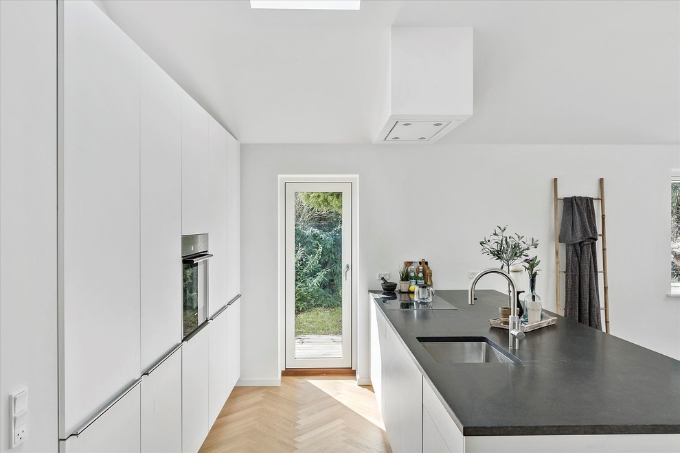 Foto på ett mellanstort minimalistiskt svart parallellkök, med en enkel diskho, släta luckor, vita skåp, integrerade vitvaror, ljust trägolv, en halv köksö och beiget golv