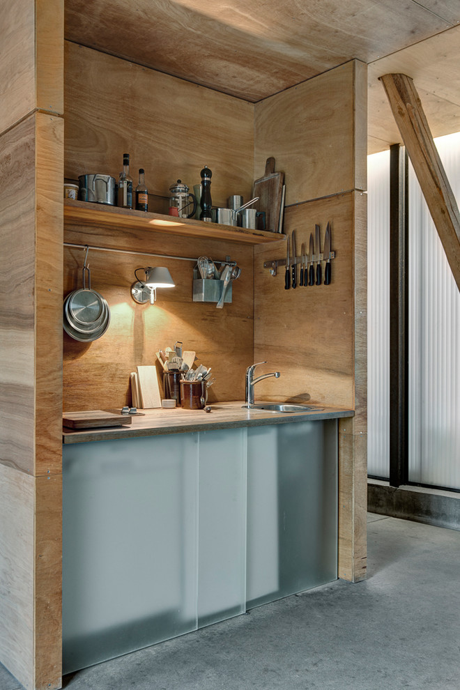 Aménagement d'une cuisine montagne en bois clair avec un évier 1 bac, un placard sans porte, une crédence en bois, sol en béton ciré, un sol gris et un plan de travail gris.