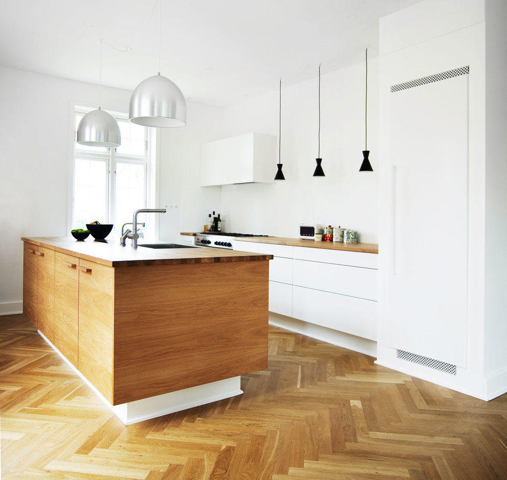 Design ideas for a contemporary galley kitchen in Odense with a submerged sink, flat-panel cabinets, white cabinets, white splashback, stainless steel appliances, medium hardwood flooring, an island and brown floors.