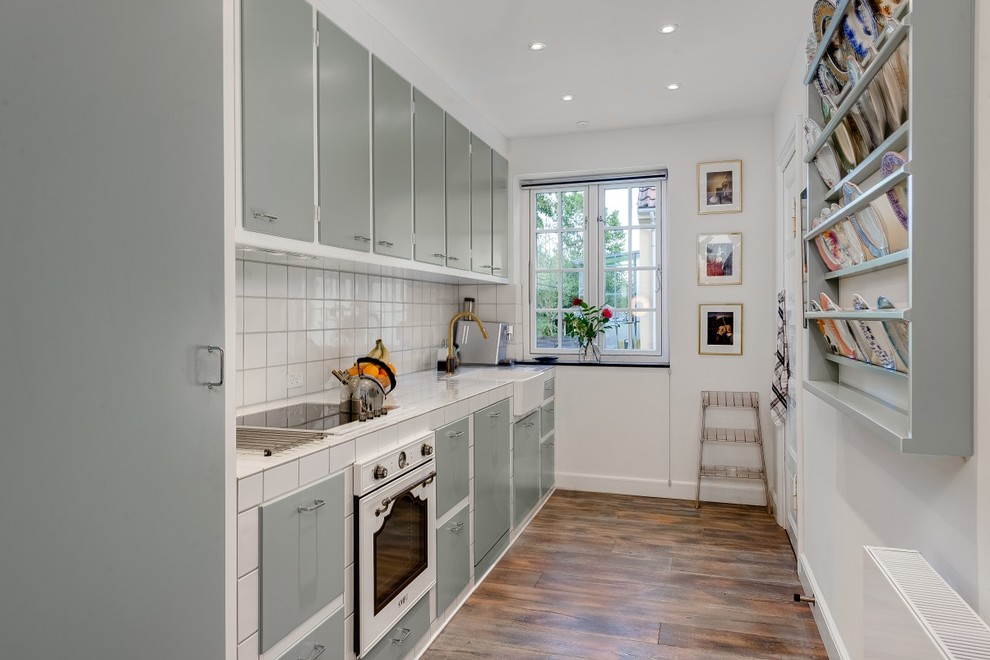 Exemple d'une cuisine linéaire scandinave fermée et de taille moyenne avec un placard à porte plane, des portes de placard grises, plan de travail carrelé et une crédence blanche.