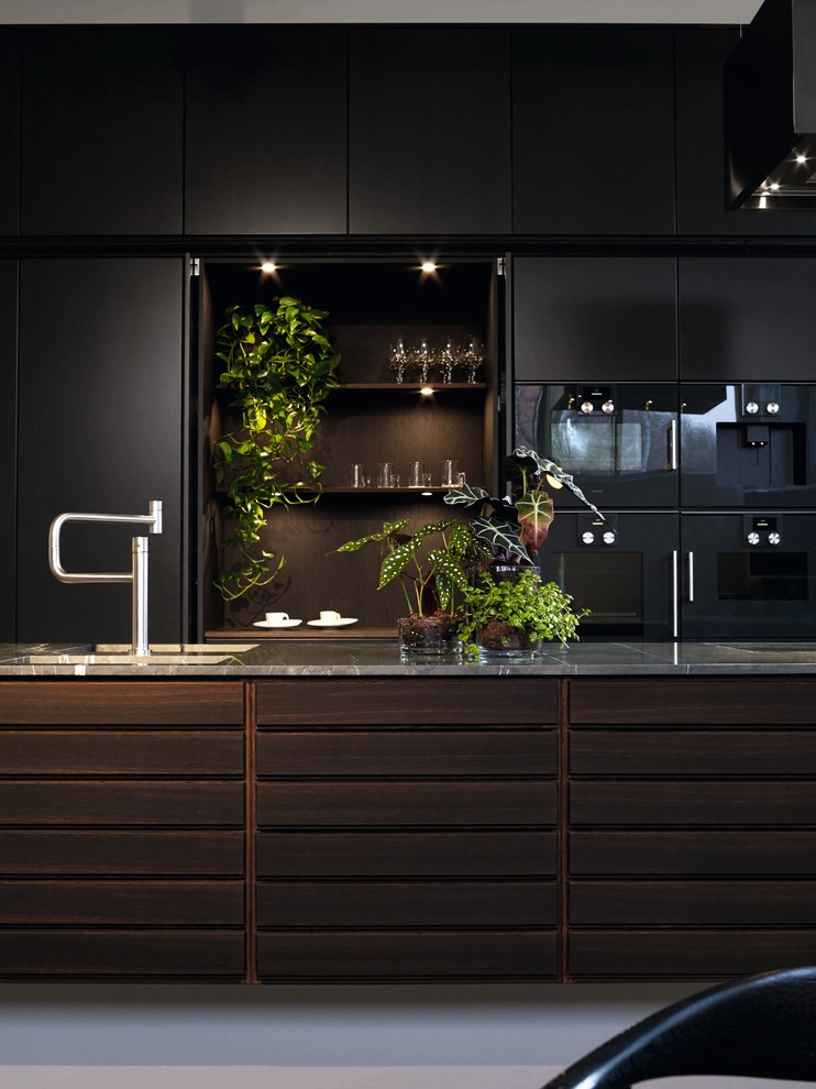 Cette photo montre une cuisine ouverte parallèle moderne en bois foncé avec un placard à porte plane, plan de travail en marbre, un électroménager noir, îlot et un plan de travail gris.