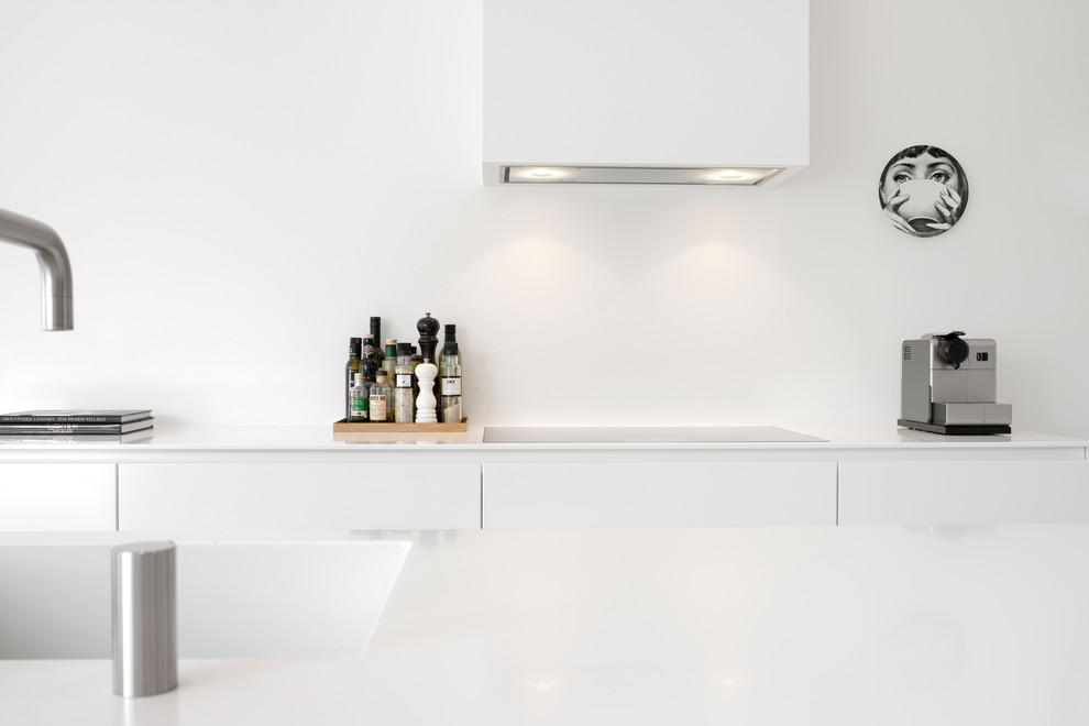 Skandinavisk inredning av ett vit vitt kök med öppen planlösning, med släta luckor, vita skåp, svarta vitvaror och en köksö