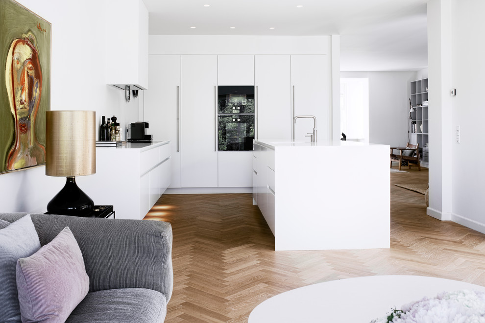 Свежая идея для дизайна: кухня-гостиная в скандинавском стиле с плоскими фасадами, белыми фасадами, черной техникой, островом и белой столешницей - отличное фото интерьера