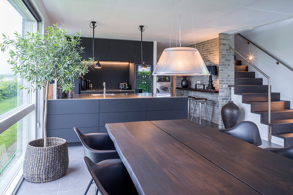 Пример оригинального дизайна: параллельная кухня-гостиная в стиле модернизм с накладной мойкой, плоскими фасадами, черными фасадами, столешницей из нержавеющей стали, черным фартуком, островом и серым полом