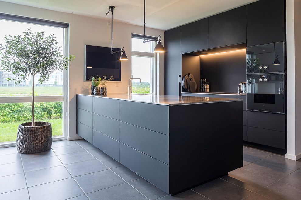Modern inredning av ett kök, med svarta vitvaror, en enkel diskho, släta luckor, svarta skåp, svart stänkskydd, en halv köksö och grått golv