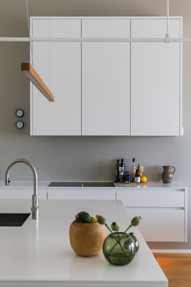 Imagen de cocina escandinava con armarios con paneles lisos, puertas de armario blancas, electrodomésticos negros, suelo de madera en tonos medios y una isla