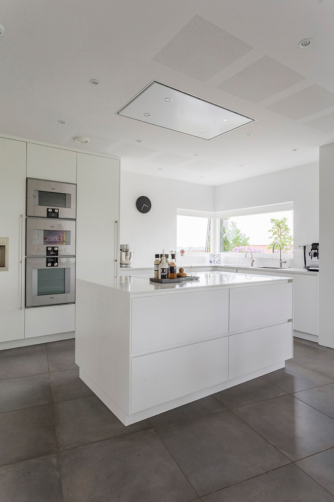 Idéer för ett modernt l-kök, med släta luckor, vita skåp, rostfria vitvaror, en köksö och grått golv