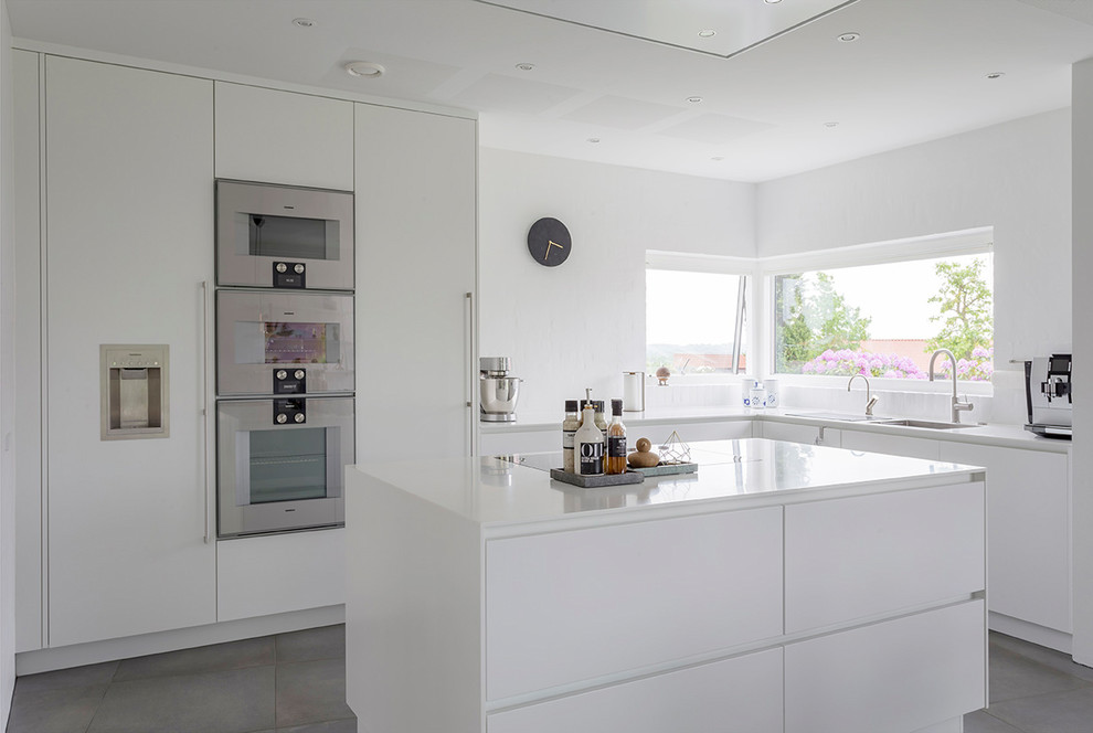 Cette image montre une cuisine design en L avec un placard à porte plane, des portes de placard blanches, un électroménager en acier inoxydable, îlot et un sol gris.