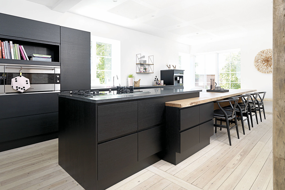 Immagine di una grande cucina design con ante lisce, ante nere, top in legno, elettrodomestici in acciaio inossidabile, parquet chiaro e lavello a vasca singola