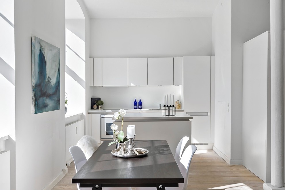 Inredning av ett minimalistiskt mellanstort linjärt kök och matrum, med släta luckor, vita skåp, vitt stänkskydd, integrerade vitvaror, ljust trägolv, beiget golv och en köksö