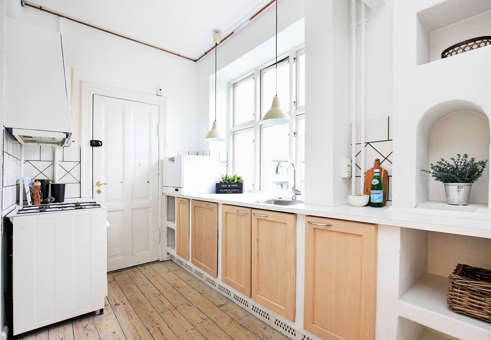 Photo of a scandi galley enclosed kitchen in Copenhagen with a submerged sink, shaker cabinets, medium wood cabinets, white splashback, white appliances, medium hardwood flooring and brown floors.