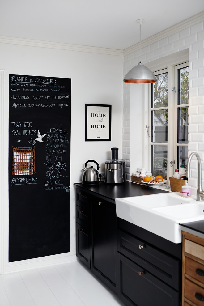 Foto på ett lantligt kök, med en rustik diskho, luckor med infälld panel, svarta skåp, vitt stänkskydd, stänkskydd i tunnelbanekakel och målat trägolv