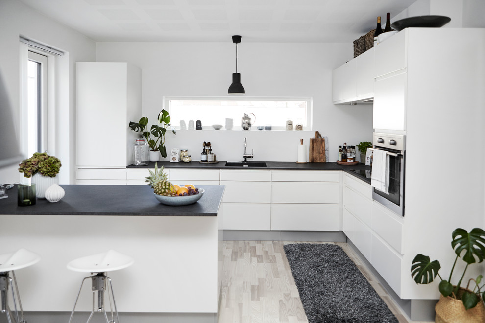 Nordische Küche in L-Form mit flächenbündigen Schrankfronten, weißen Schränken, Küchengeräten aus Edelstahl, hellem Holzboden und Halbinsel in Wiltshire