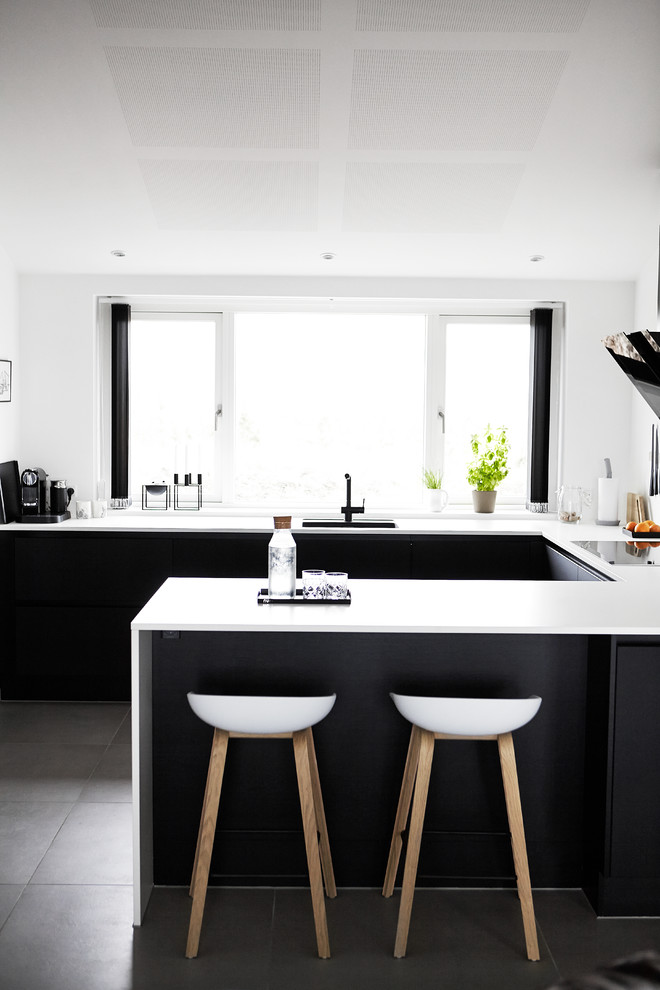 На фото: п-образная кухня-гостиная среднего размера в скандинавском стиле с врезной мойкой, полуостровом, плоскими фасадами, столешницей из ламината, полом из керамической плитки и черно-белыми фасадами с