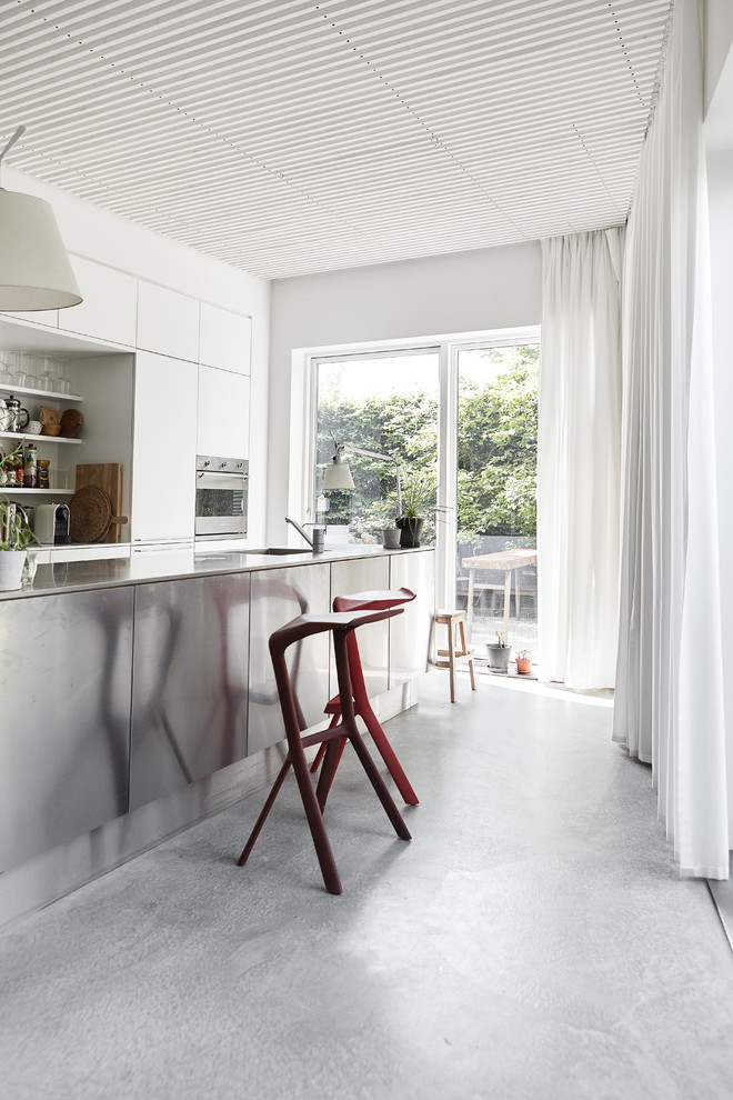 Inredning av ett modernt stort kök, med släta luckor, vita skåp, betonggolv, en köksö och grått golv