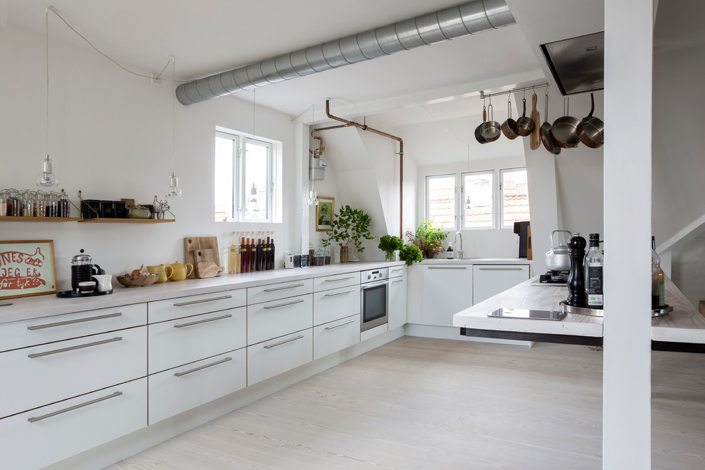 Bild på ett avskilt, stort skandinaviskt l-kök, med en nedsänkt diskho, släta luckor, vita skåp, bänkskiva i kvartsit, rostfria vitvaror, ljust trägolv och en köksö