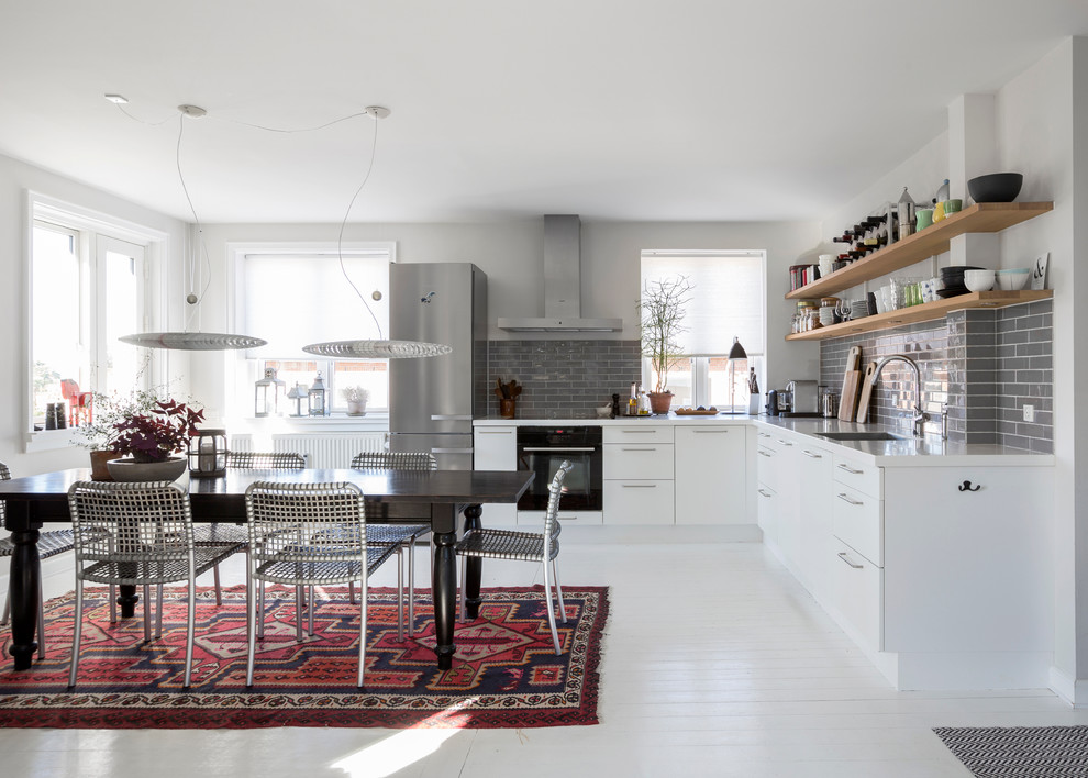 Foto på ett mellanstort funkis kök, med en integrerad diskho, släta luckor, vita skåp, laminatbänkskiva, grått stänkskydd, stänkskydd i porslinskakel, svarta vitvaror och målat trägolv