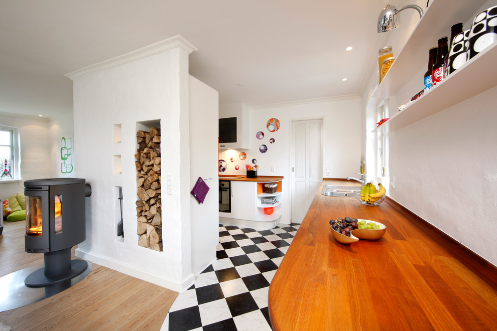 На фото: угловая кухня-гостиная среднего размера в стиле фьюжн с накладной мойкой, плоскими фасадами, белыми фасадами, деревянной столешницей, черной техникой и полом из линолеума без острова