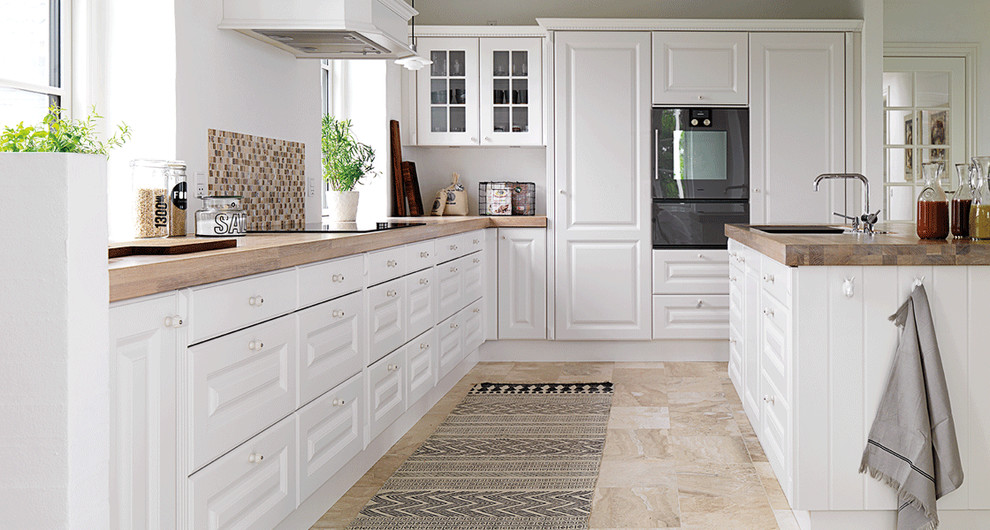 Enclosed kitchen - large farmhouse galley marble floor enclosed kitchen idea in Copenhagen with a drop-in sink, raised-panel cabinets, white cabinets, wood countertops, multicolored backsplash, mosaic tile backsplash, black appliances and an island