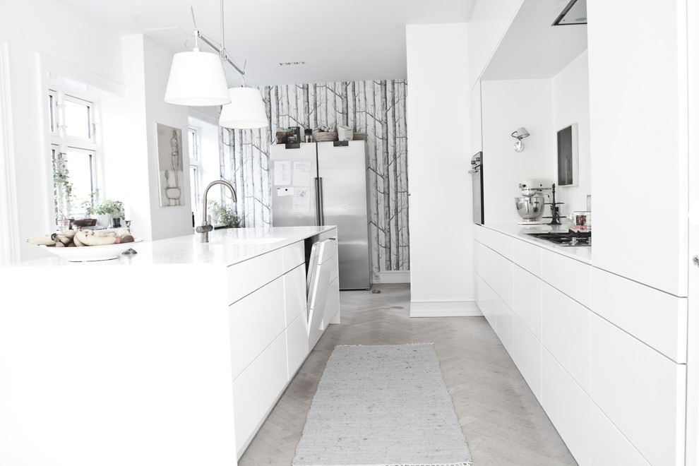 Foto på ett nordiskt kök, med släta luckor, vita skåp, ljust trägolv, en köksö och grått golv