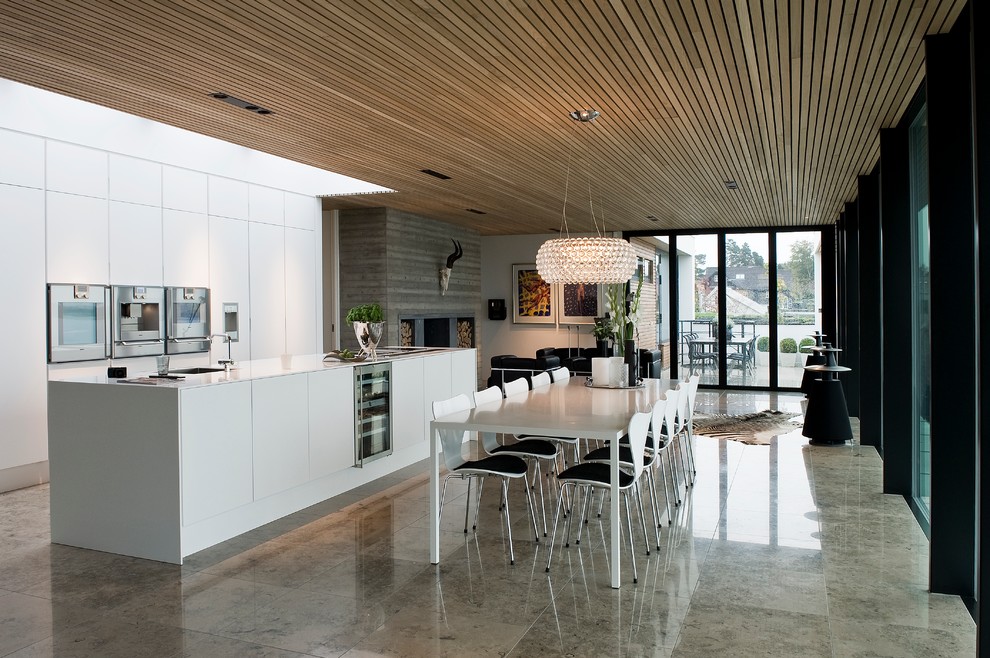 Foto på ett minimalistiskt kök och matrum, med en undermonterad diskho, släta luckor, vita skåp, rostfria vitvaror och en köksö