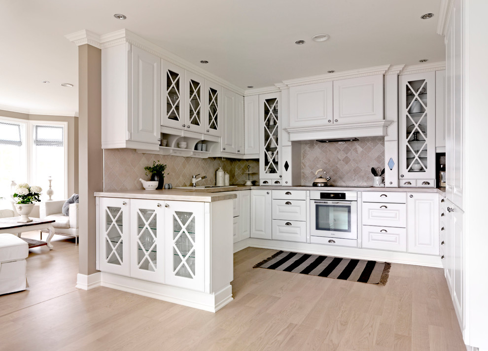 Klassisk inredning av ett avskilt, stort u-kök, med en enkel diskho, luckor med upphöjd panel, vita skåp, granitbänkskiva, beige stänkskydd, stänkskydd i keramik, rostfria vitvaror och ljust trägolv