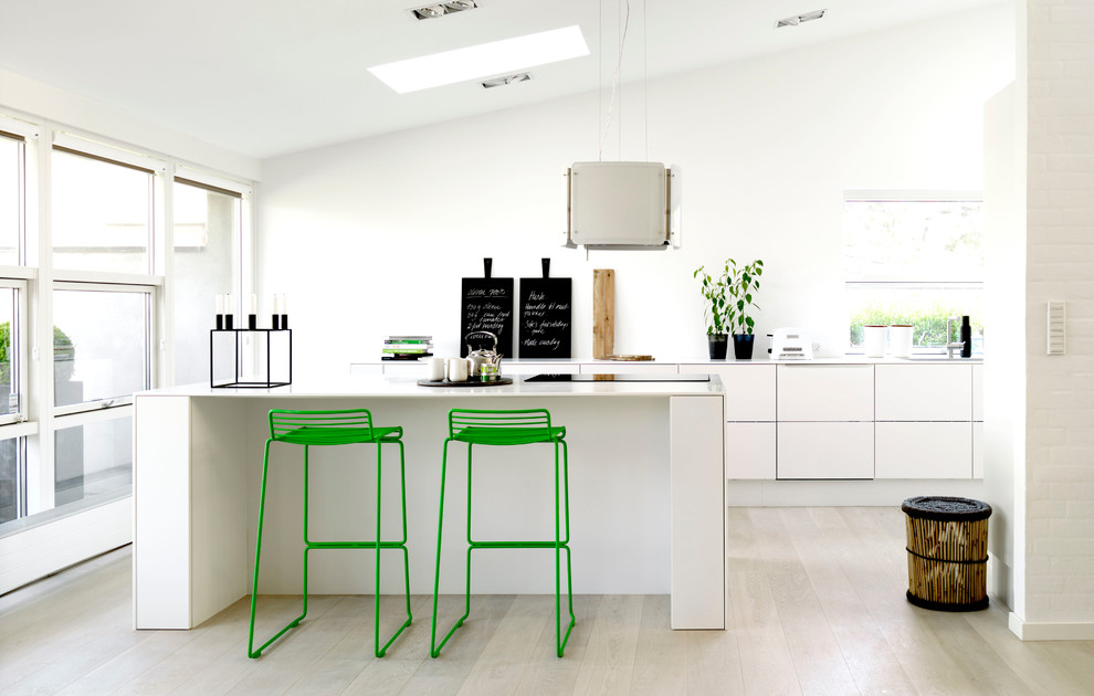 This is an example of a large scandinavian galley open plan kitchen in Aarhus with flat-panel cabinets, white cabinets, laminate countertops, light hardwood flooring and an island.