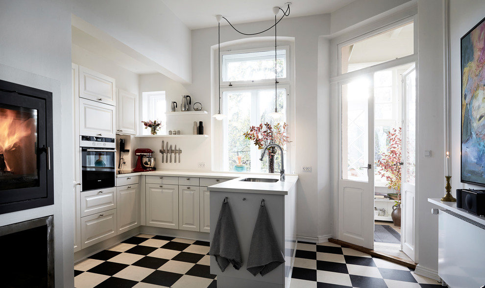 На фото: п-образная кухня в скандинавском стиле с врезной мойкой, фасадами с выступающей филенкой, белыми фасадами и полуостровом с